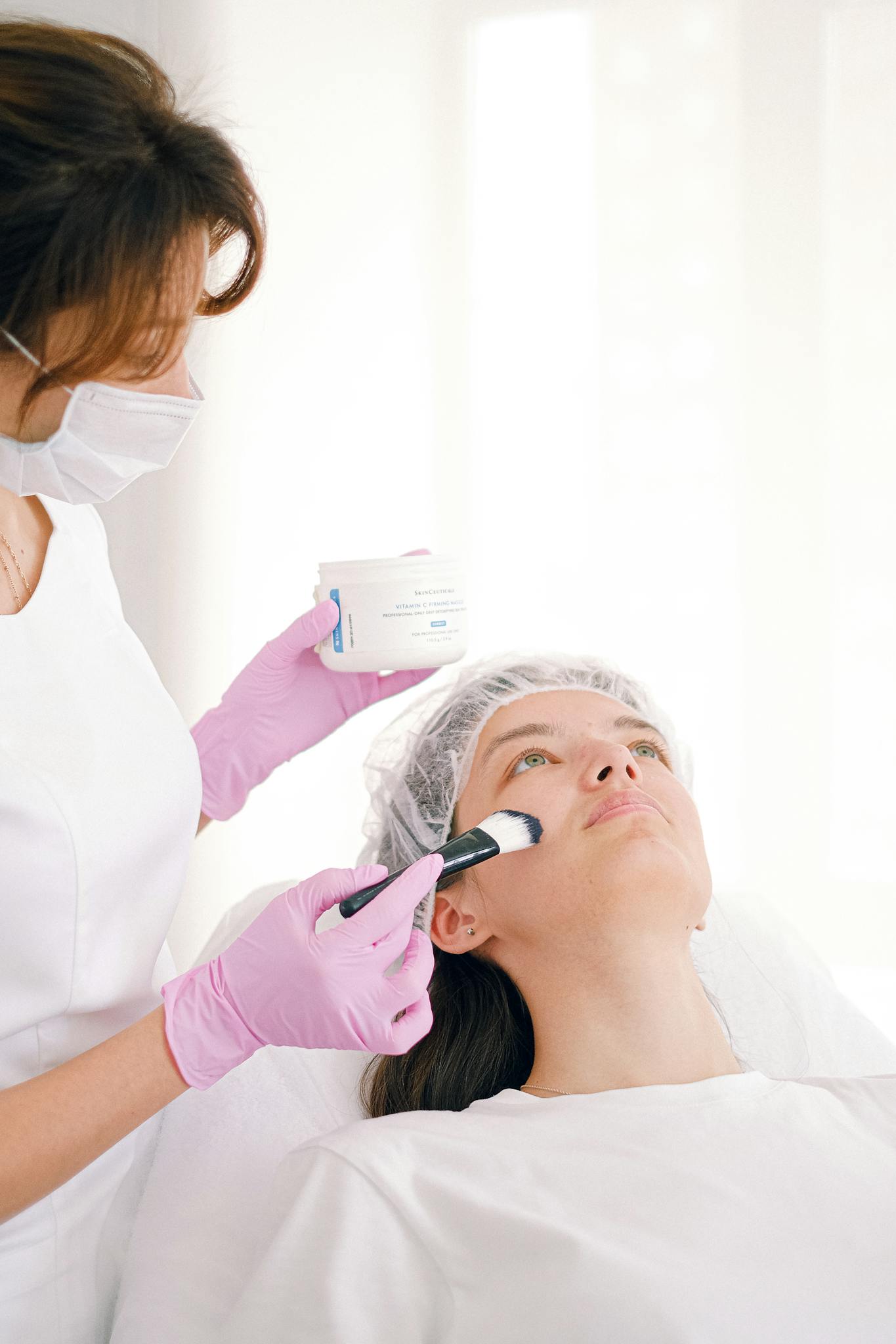 Beautician applying facial treatment to a patient in a modern skincare clinic setting.