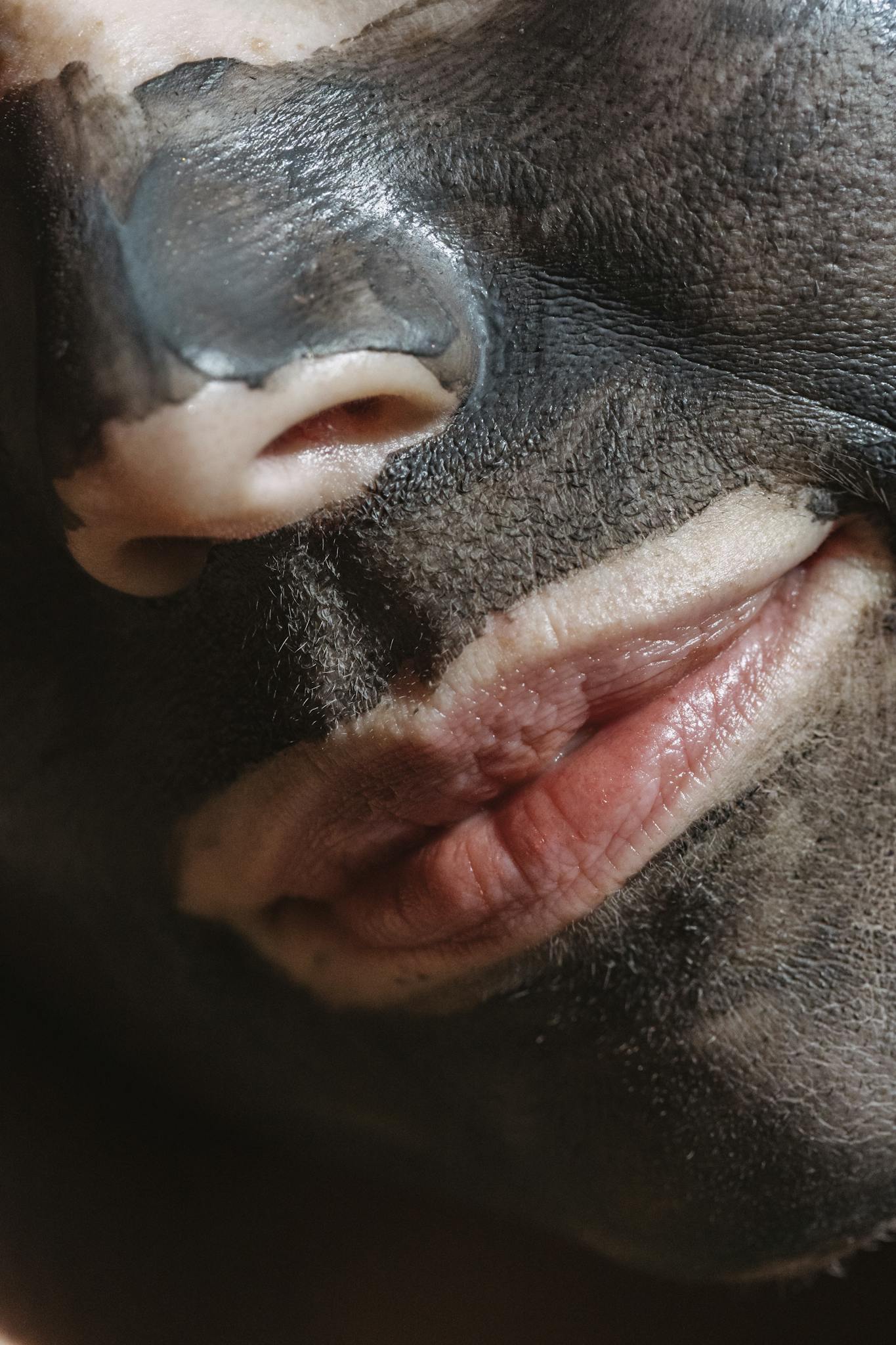 Closeup of crop calm unrecognizable woman with cleansing clay mask doing facial procedure in daylight