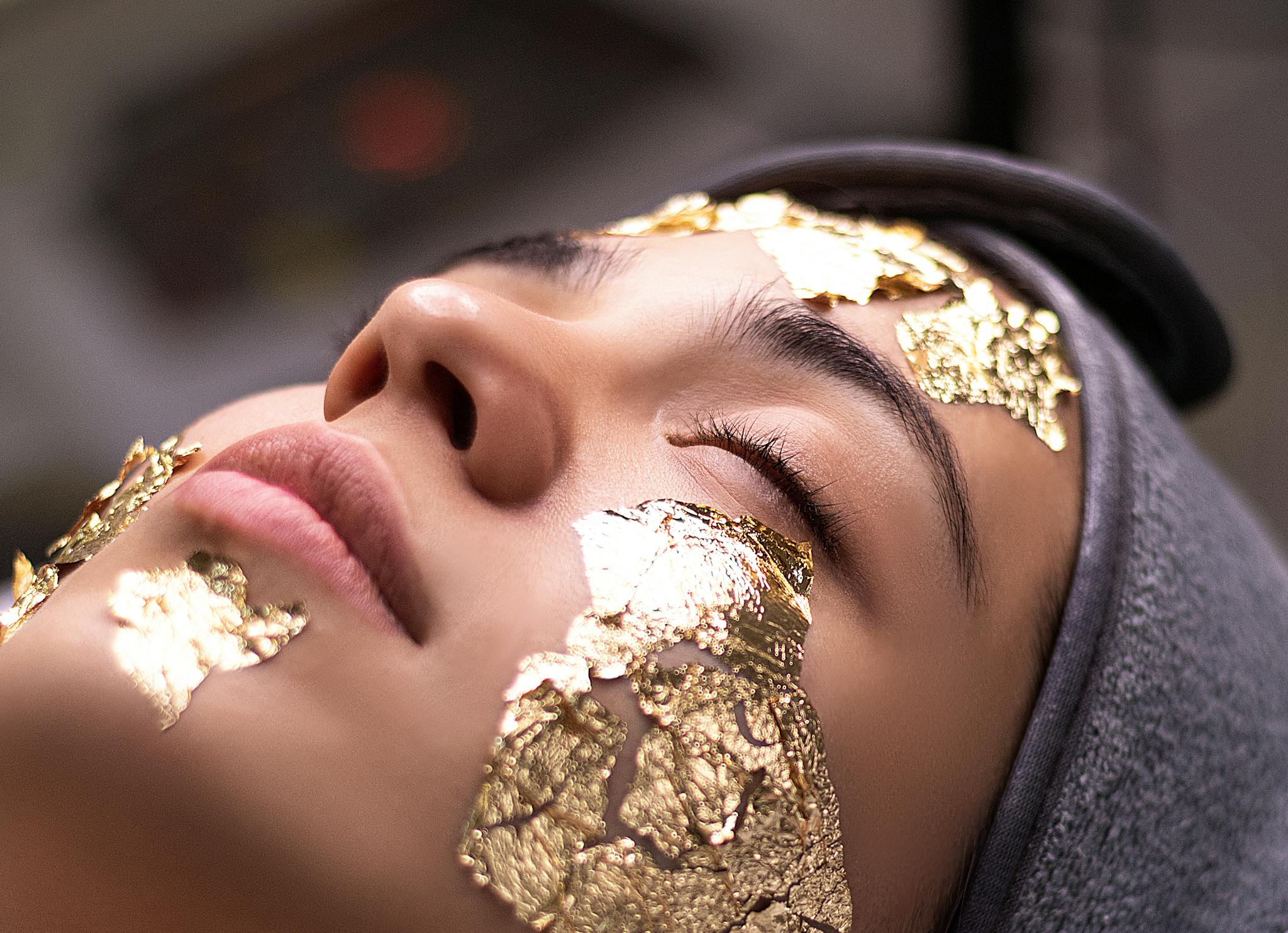 Close-up of a woman's face with gold foil on her skin for luxurious skincare treatment.