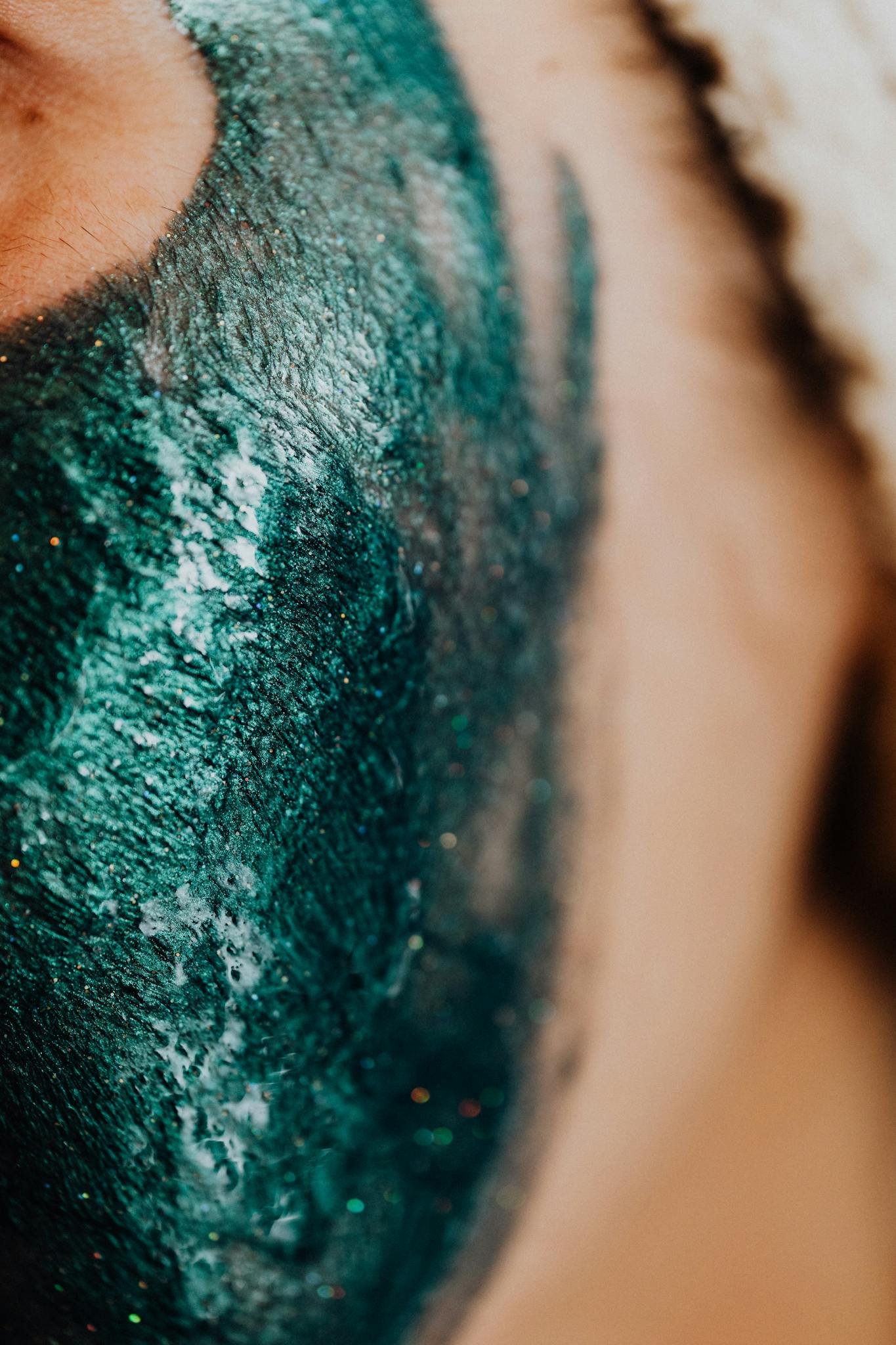 Close-up shot of a woman's face with a glittery green face mask, highlighting skincare and self-care practices.